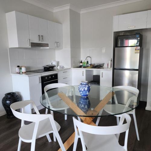 a kitchen with a glass table and white chairs at Rooms at Gables in a modern home in Annangrove
