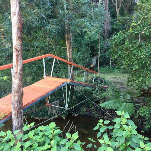 a wooden bridge over a river in a forest at Nature Retreat & Artists Studio 90mins from Sydney in Spencer