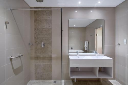 uma casa de banho com um lavatório e uma cabina de duche em vidro. em Protea Hotel by Marriott Pretoria Hatfield em Pretoria
