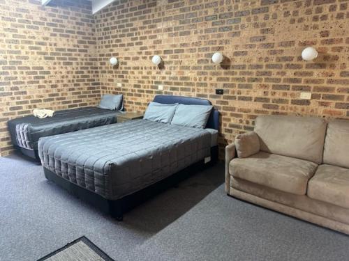 a bedroom with two beds and a couch and a brick wall at Clock Tower Motor Inn in Coonabarabran