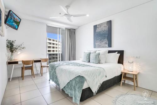 a white bedroom with a bed and a desk and a window at 602 Harbour Lights with Ocean Views in Cairns