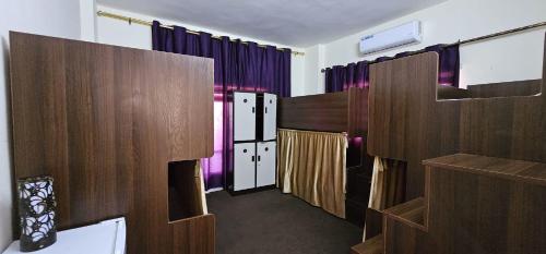 Habitación con cortinas moradas y divisores de madera. en Pizza Street Hostel, en Áqaba