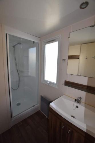 La salle de bains est pourvue d'une douche et d'un lavabo blanc. dans l'établissement Mobil-home 40, à Samoëns