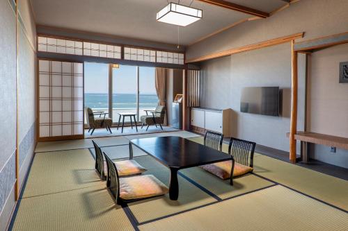 a living room with a table and chairs and the ocean at Hotel Sanrakuso in Shirahama