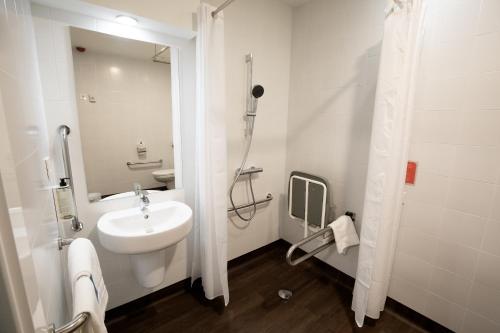 Travelodge Madrid Metropolitano في مدريد: حمام أبيض مع حوض ودش