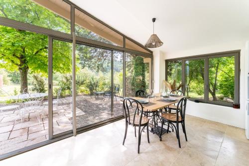 a dining room with a table and chairs and large windows at Maison Marvic, Le Tilleul T3 in Apt