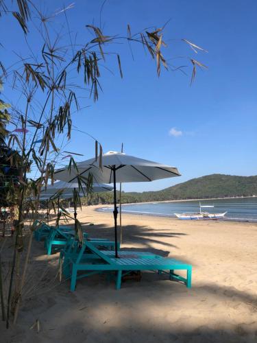 two picnic tables and an umbrella on a beach at Zhaya's Beach & Cottages in El Nido