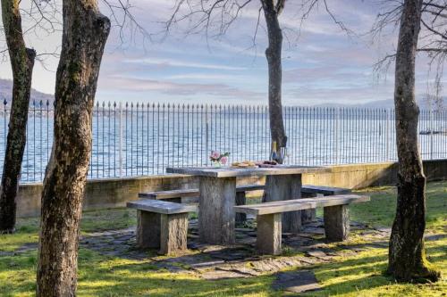 a picnic table with benches in front of the water at Villa Lago Maggiore in Lesa