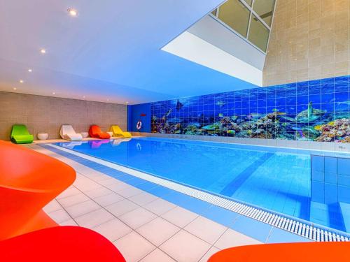 a large swimming pool in a hotel with colourful chairs at Novotel Zurich City West in Zürich