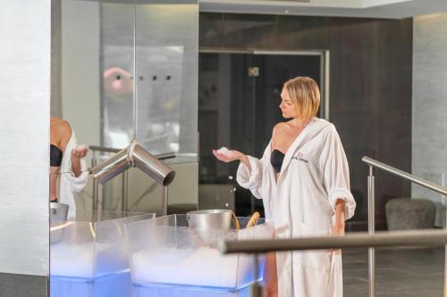 a woman in a bathrobe standing in front of a mirror at Hotel Mioni Royal San in Montegrotto Terme