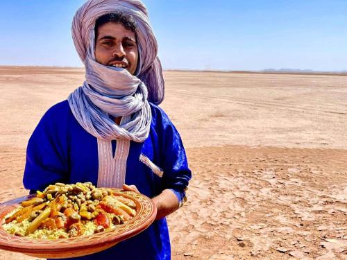 a man holding a plate of food in the desert at Auberge Sahara Iriki & Désert Tours in Foum Zguid