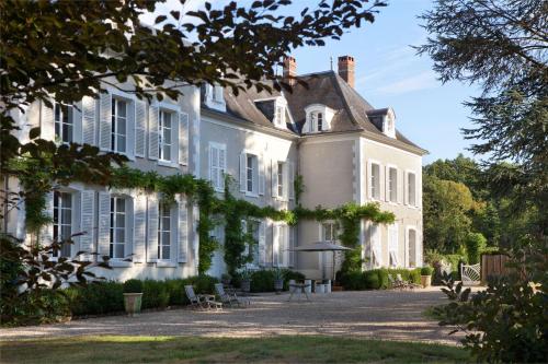 une grande maison blanche avec des chaises et un parasol dans l'établissement Chateau De La Resle - Design Hotels, à Montigny-la-Resle