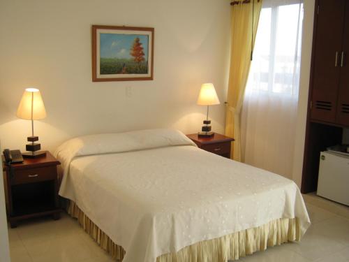 a bedroom with a white bed with two lamps on tables at Hotel Sol Dorado in Villavicencio