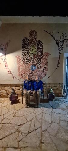 two men sitting on a bench in front of a wall at Hotel Pansy in Ksar Ghilane