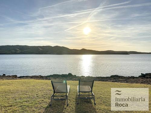 two chairs sitting on the grass near a body of water at P82. Apartamento marinero con Wifi y aire acondicionado in Fornells