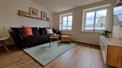 a living room with a black couch and two windows at Urlaubsnest Millstatt in 5 Minuten am Millstätter See in Millstatt