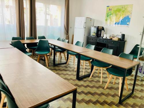a classroom with wooden tables and green chairs at Hôtel Le Gambetta in Vias