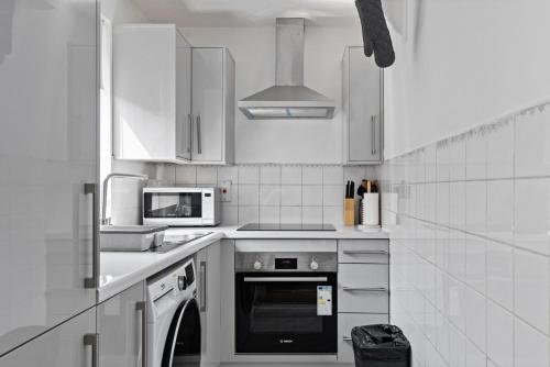 a white kitchen with a stove and a microwave at Shades of white in Mill Hill in Hendon