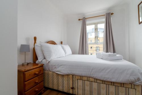 um quarto com uma cama com lençóis brancos e uma janela em GuestReady - Parkside getaway in Britannia Village em Londres