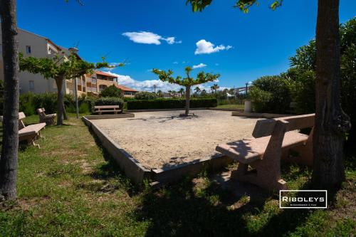 a park with benches and a tree in the sand at Vias-Plage - Appartement climatisé avec piscine face à la mer in Vias