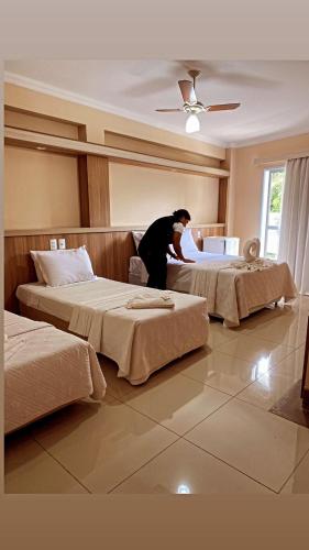 una persona haciendo dos camas en una habitación de hotel en Hotel Lux, en Poços de Caldas
