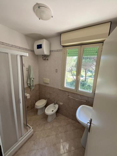 bagno con due servizi igienici, lavandino e finestra di Residence Verde Pineta a Principina a Mare