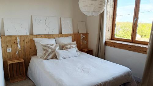 sypialnia z białym łóżkiem z poduszkami i oknem w obiekcie Maison ecologique en paille w mieście La Chapelle-Enchérie