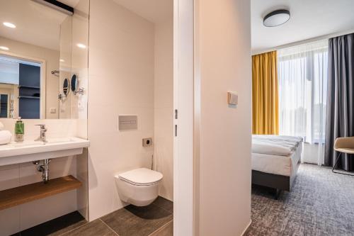 a bathroom with a toilet sink and a bed at EA Congress Hotel Aldis in Hradec Králové