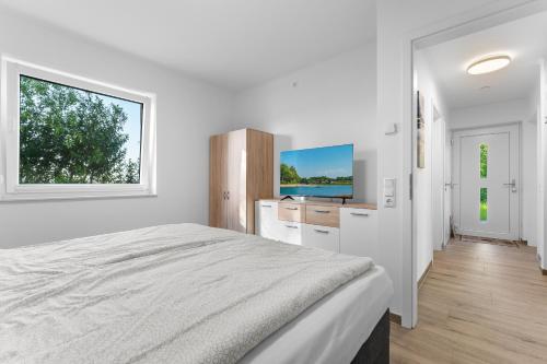 a white bedroom with a bed and a flat screen tv at Niewoh Ferienhaus Wiesenblick,Ammerland, Conneforde in Wiefelstede