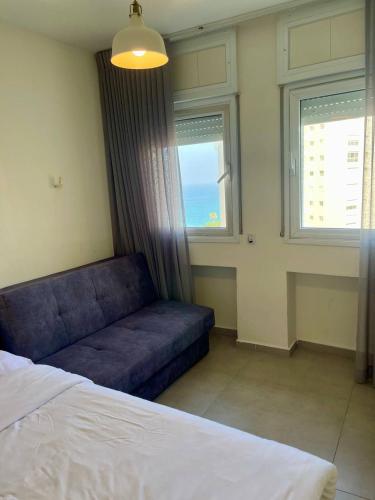 a bedroom with a blue couch and two windows at Netanya Sea Studio in Netanya
