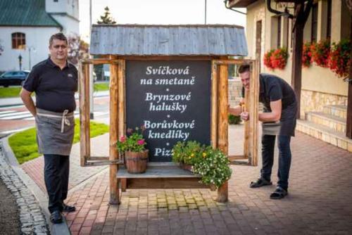 two men standing in front of a sign with flowers at Penzion a restaurace Staré Časy in Horní Bečva