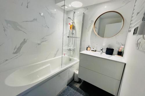 La salle de bains blanche est pourvue d'une baignoire, d'un lavabo et d'un miroir. dans l'établissement Cosy flat 2 steps from the port 4pers, à Gujan-Mestras