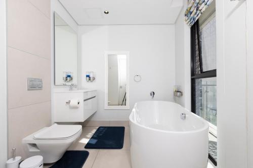 a white bathroom with a tub and a toilet at The Executive Apartment in Ellipse Waterfall City in Midrand