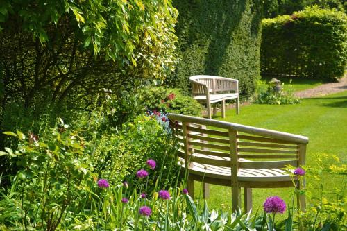 dos bancos sentados en un jardín con flores en The Cottage Guest House, en Bishops Stortford