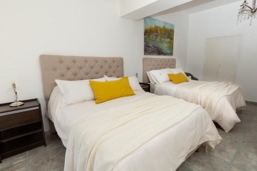 a bedroom with two beds with white sheets and yellow pillows at La Santa Hotel Boutique in Mendiolaza