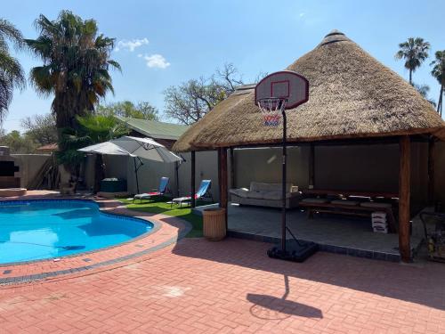 a pool with a basketball hoop and a thatch roof at Mokapelo Life Style Guest House in Bela-Bela