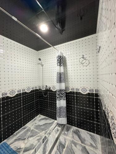 ein Bad mit einer Dusche mit schwarzen und weißen Fliesen in der Unterkunft Shodmon Guesthouse in Jizzax