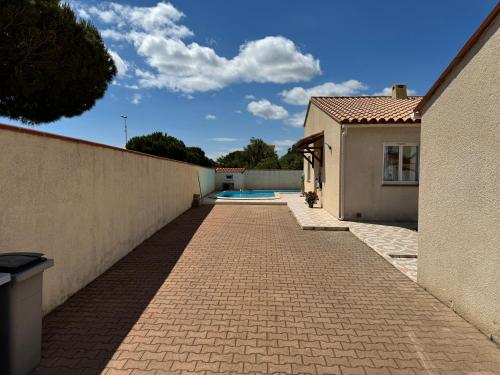 une allée en briques à côté d'une maison et d'une piscine dans l'établissement Villa la lagune piscine et spa privés 8 Couchages parking privé et borne de recharge électrique, au Barcarès