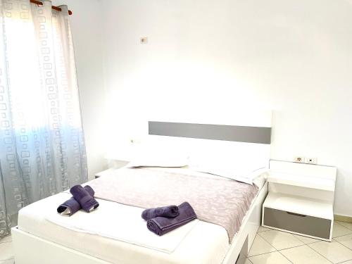 a white bed with two purple slippers on it at Ernest Apartments in Sarandë