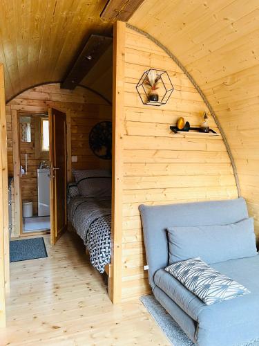 - une chambre dans une cabane en rondins avec un lit et un canapé dans l'établissement Aux Étangs de Jourgnac - Cabane MégaPod, à Jourgnac