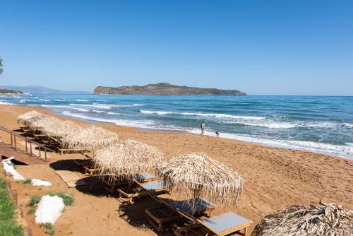 una playa con sillas y sombrillas de paja y el océano en The Mini Beach Hotel, en Stalós