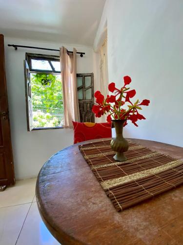 a table with a vase with red flowers on it at Apartamento no centro para Casal in Mata de Sao Joao