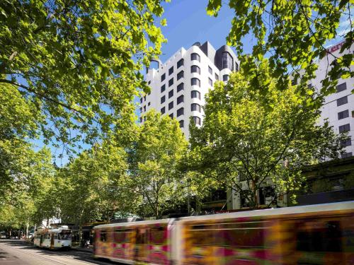 メルボルンにあるPullman Melbourne City Centreの高層ビルが立ち並ぶ街路を走るバス