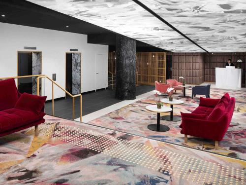 a lobby with red chairs and tables in a room at Pullman Melbourne City Centre in Melbourne