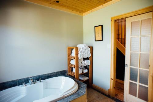 a bathroom with a white tub and a shelf of towels at Le Chalet des Coteaux in LʼAnse-Saint-Jean