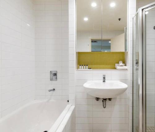 a white bathroom with a sink and a bath tub at Glenelg Oasis, Pool, Gym, Spa & Sauna, Free Parking, City Views in Glenelg
