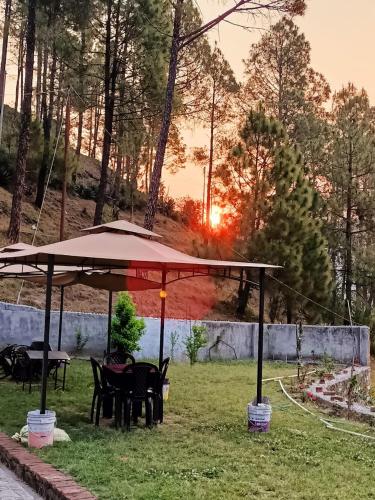 a table and chairs under an umbrella in the grass at Trails of Bheta in Kausani