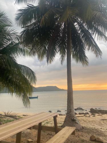 a bench under a palm tree on the beach at Lily's Beach Bungalows in Koh Rong Island