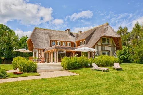 Cette grande maison est dotée d'un toit de chaume. dans l'établissement La Chaumière - Tennis & Swimming Pool - Branville, à Branville
