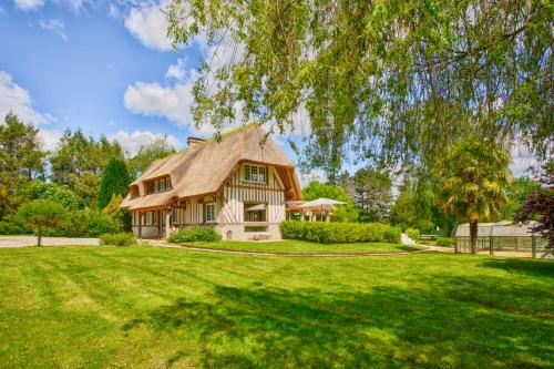 une maison avec un toit de chaume sur une pelouse verdoyante dans l'établissement La Chaumière - Tennis & Swimming Pool - Branville, à Branville